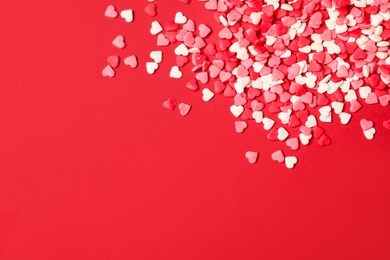Photo of Bright heart shaped sprinkles on red background, flat lay. Space for text