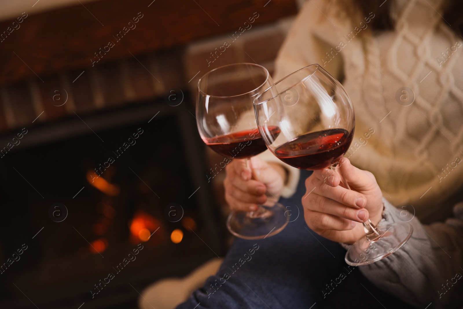 Photo of Couple with glasses of red wine near fireplace, closeup