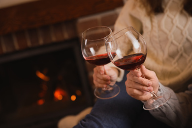 Couple with glasses of red wine near fireplace, closeup