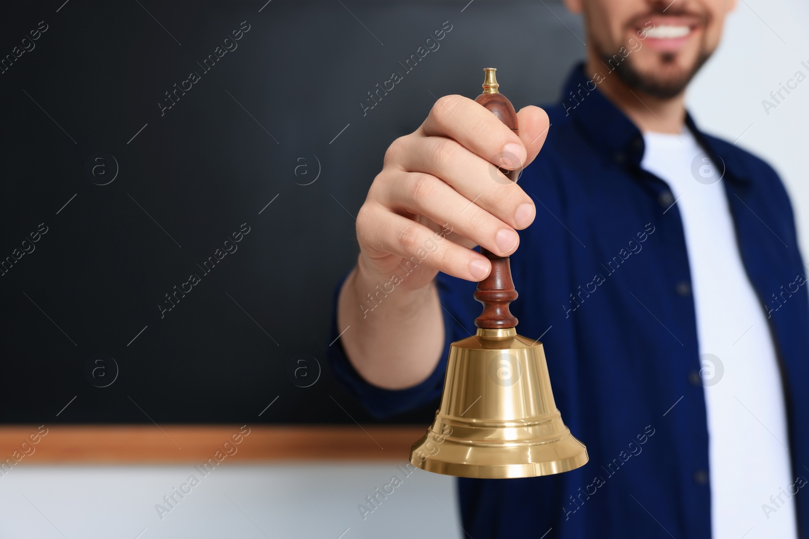 Photo of Teacher with school bell near black chalkboard, closeup. Space for text