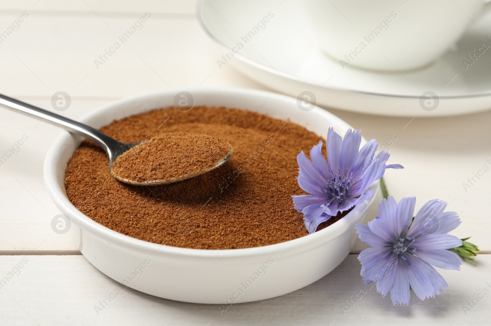 Photo of Bowl of chicory powder and flowers on white wooden table