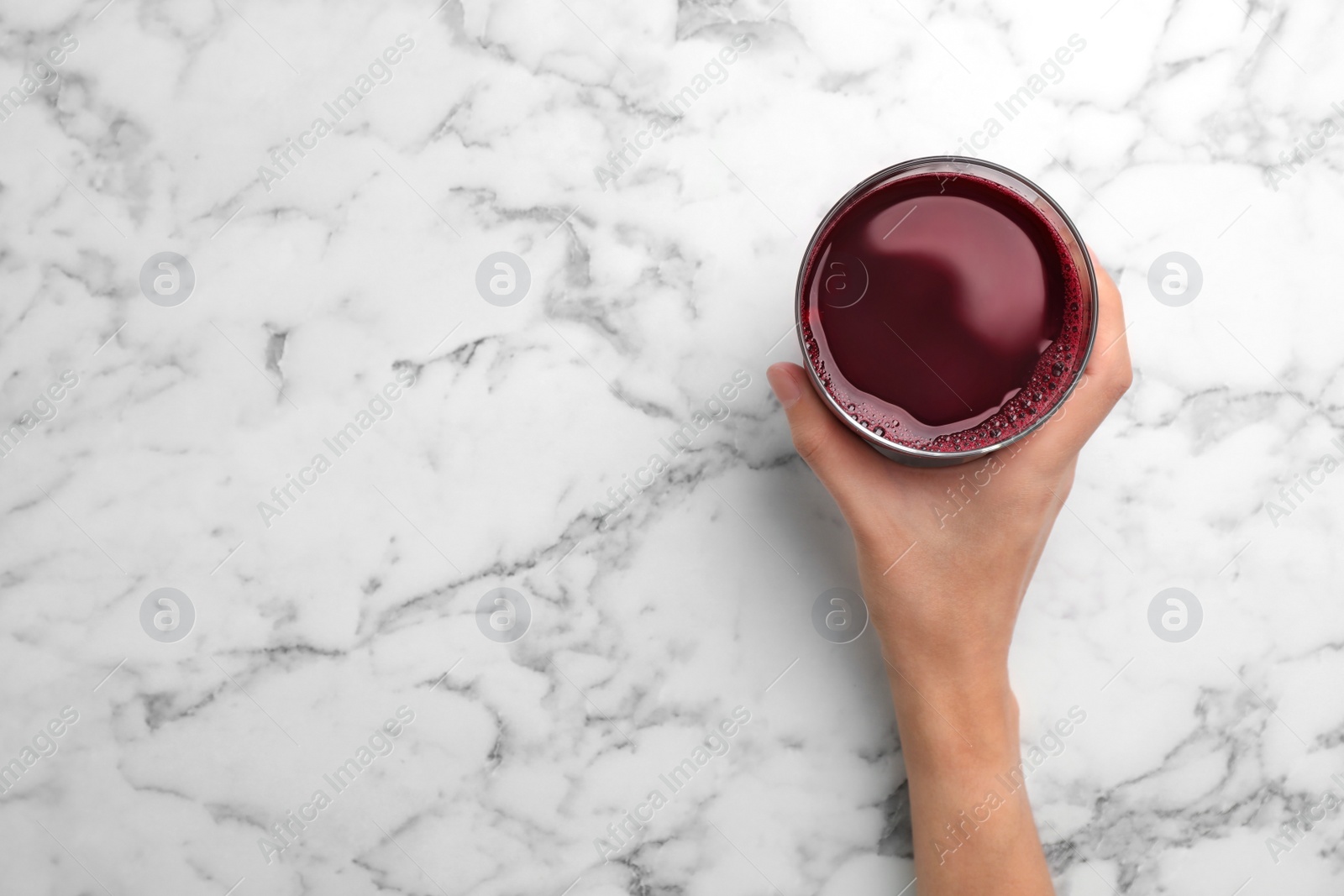 Photo of Woman holding glass with fresh beet juice on marble table, top view