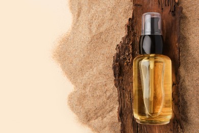 Photo of Bottle of serum and tree bark on sand against beige background, top view. Space for text