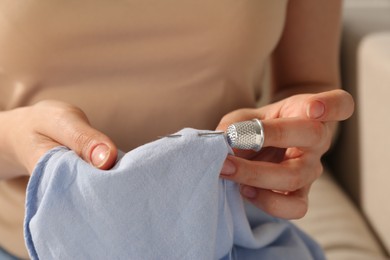 Photo of Woman sewing on light blue with thimble and needle indoors, closeup