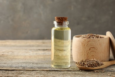 Caraway (Persian cumin) seeds and essential oil on wooden table, space for text