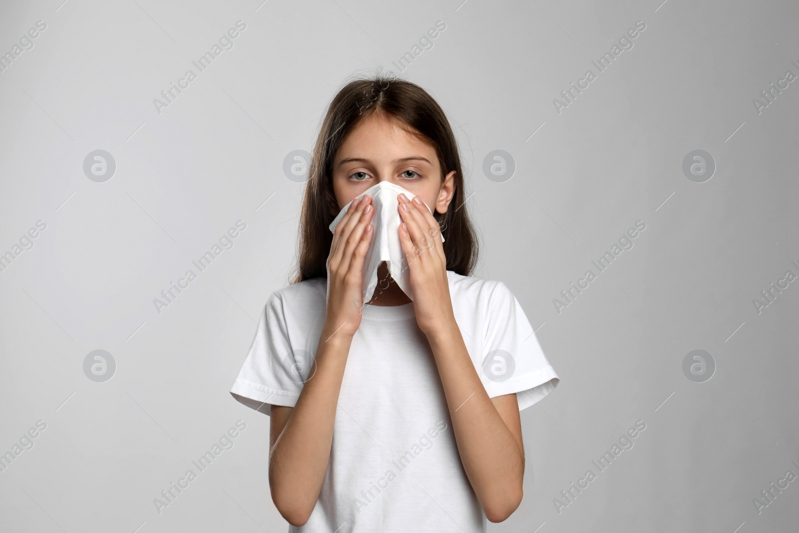 Photo of Little girl blowing nose into paper tissue on light grey background. Seasonal allergy