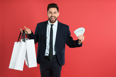 Photo of Young man with money and shopping bags on crimson background