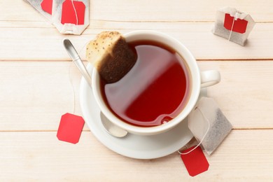 Photo of Tea bags, cup of hot beverage and spoon on light wooden table, flat lay