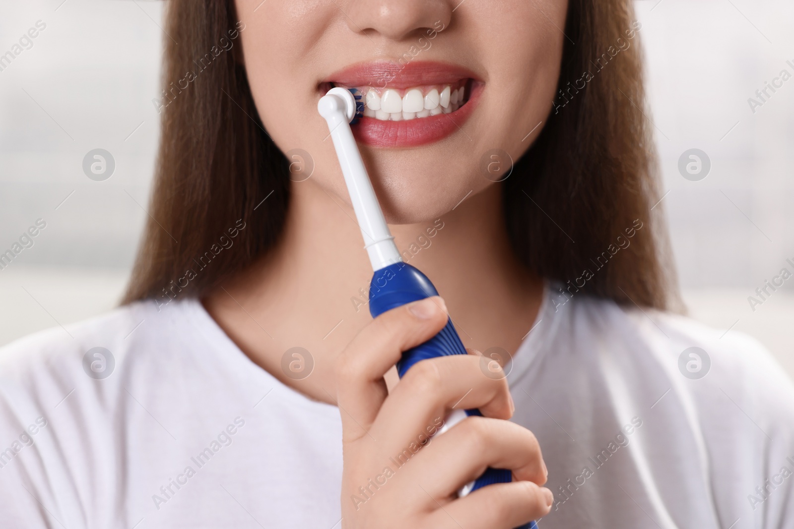 Photo of Woman brushing her teeth with electric toothbrush indoors, closeup