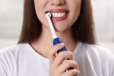 Woman brushing her teeth with electric toothbrush indoors, closeup