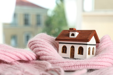 Photo of House model and pink scarf on table on blurred background, space for text. Heating efficiency