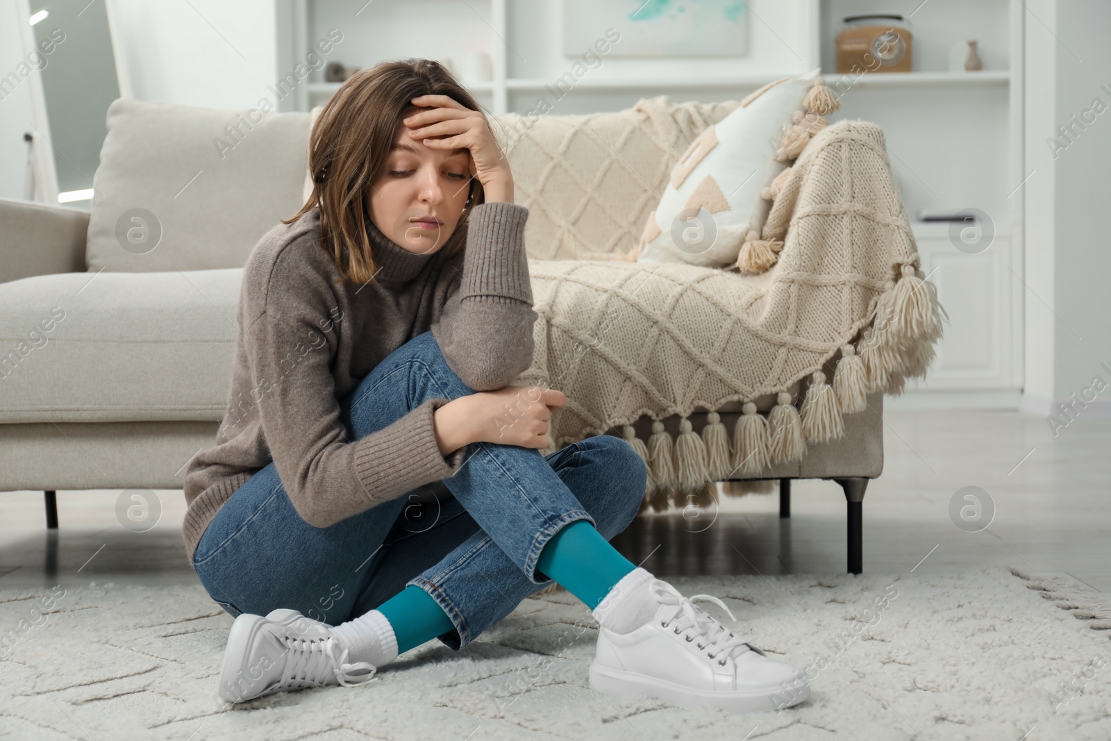 Photo of Sad young woman sitting on floor indoors, space for text