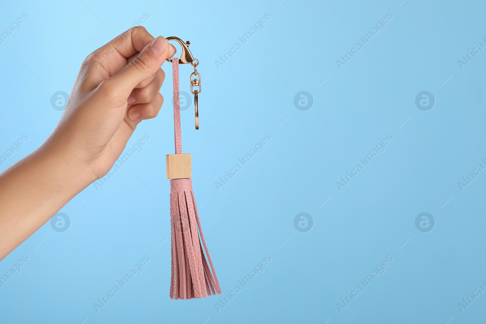 Photo of Woman holding pink leather keychain on light blue background, closeup. Space for text