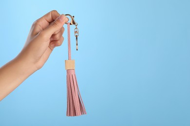 Woman holding pink leather keychain on light blue background, closeup. Space for text