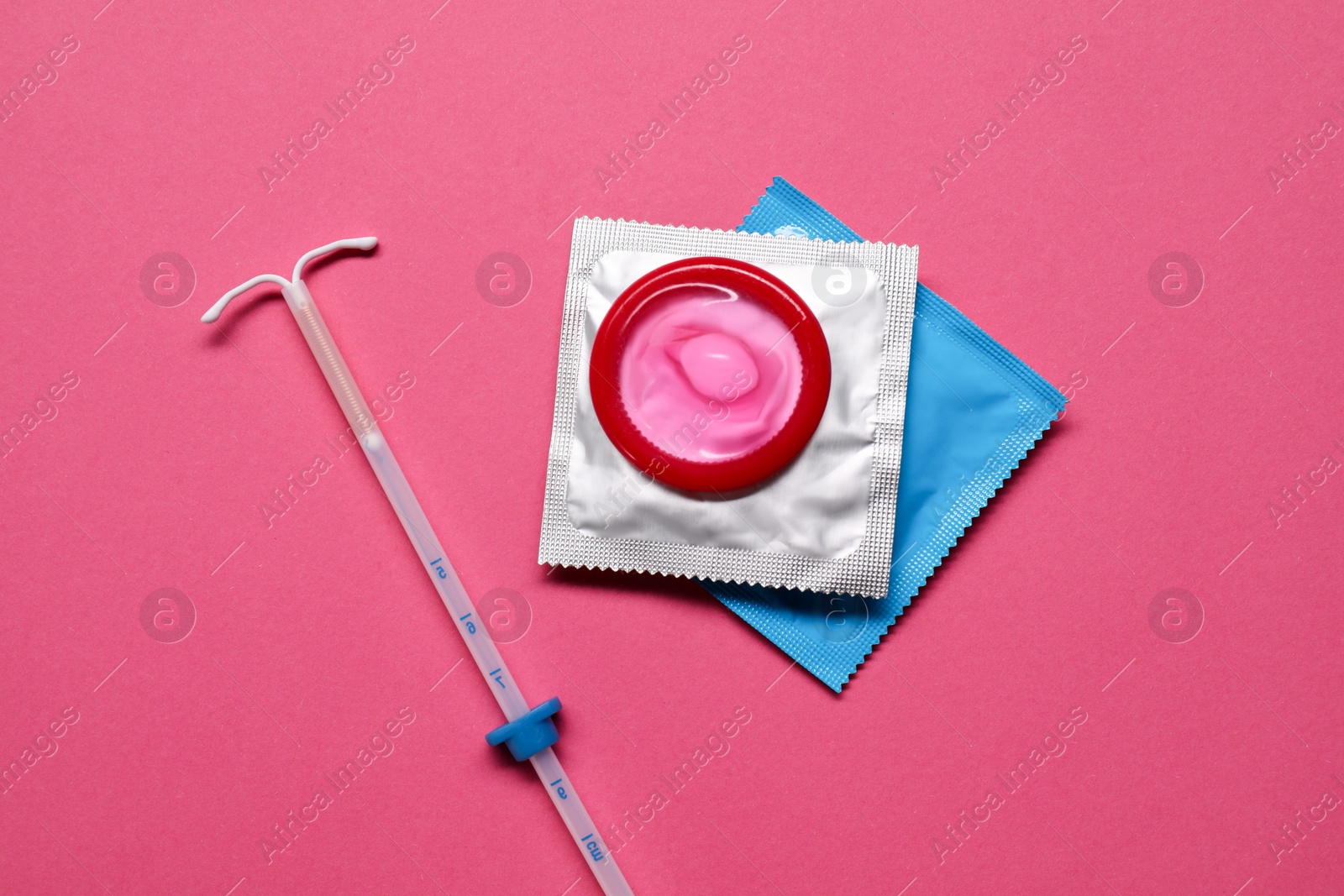 Photo of Contraception choice. Condoms and intrauterine device on magenta background, flat lay