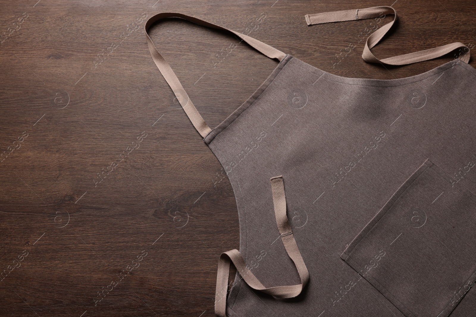 Photo of Stylish brown apron on wooden table, top view. Mockup for design