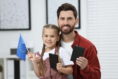 Photo of Immigration. Happy man with his daughter holding passports and flag of European Union indoors