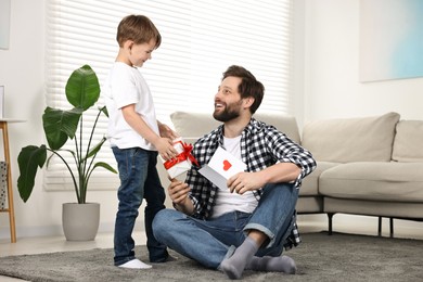 Photo of Happy Father's Day. Son giving gift box to his father with greeting card at home