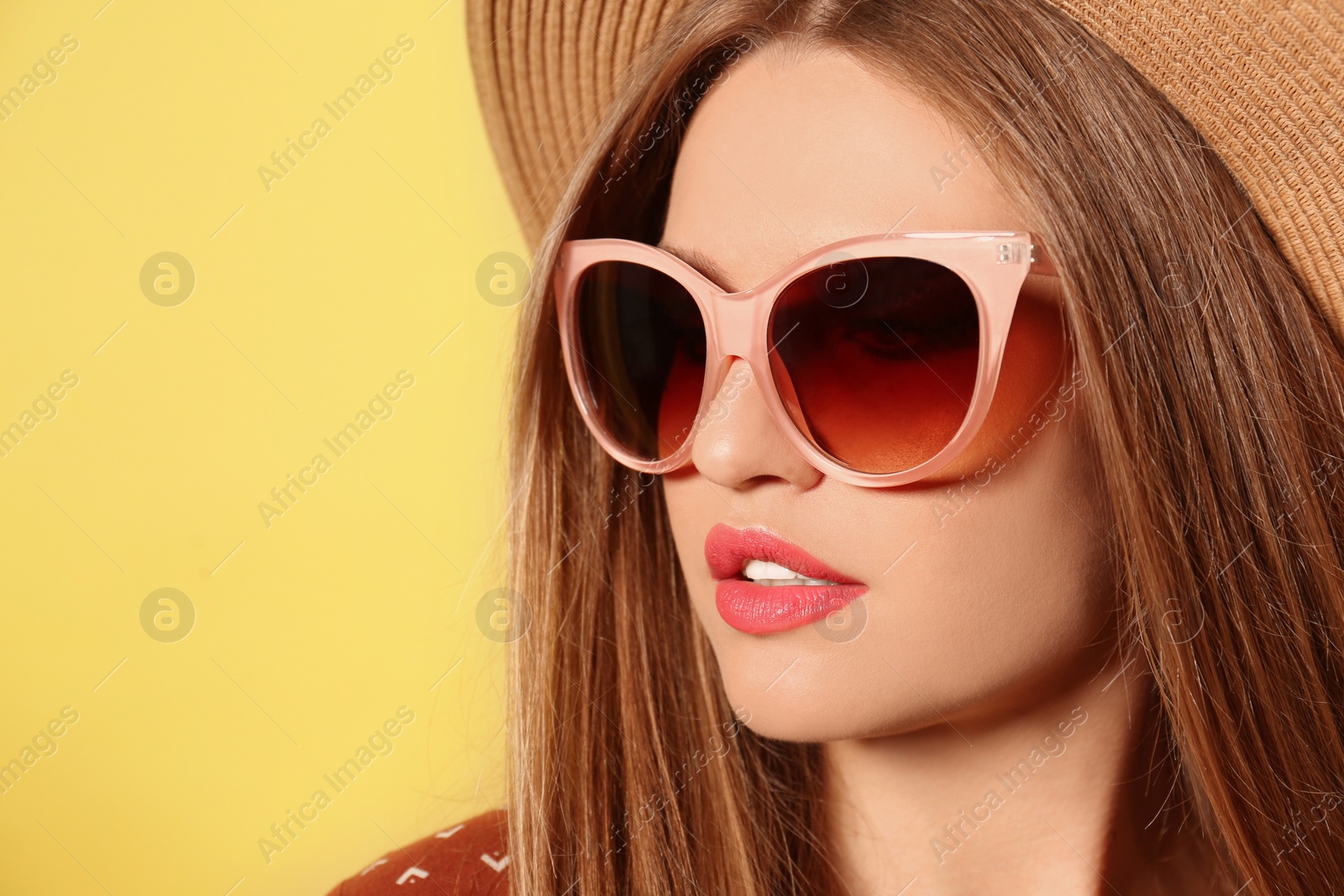 Photo of Young woman wearing stylish sunglasses and hat on yellow background