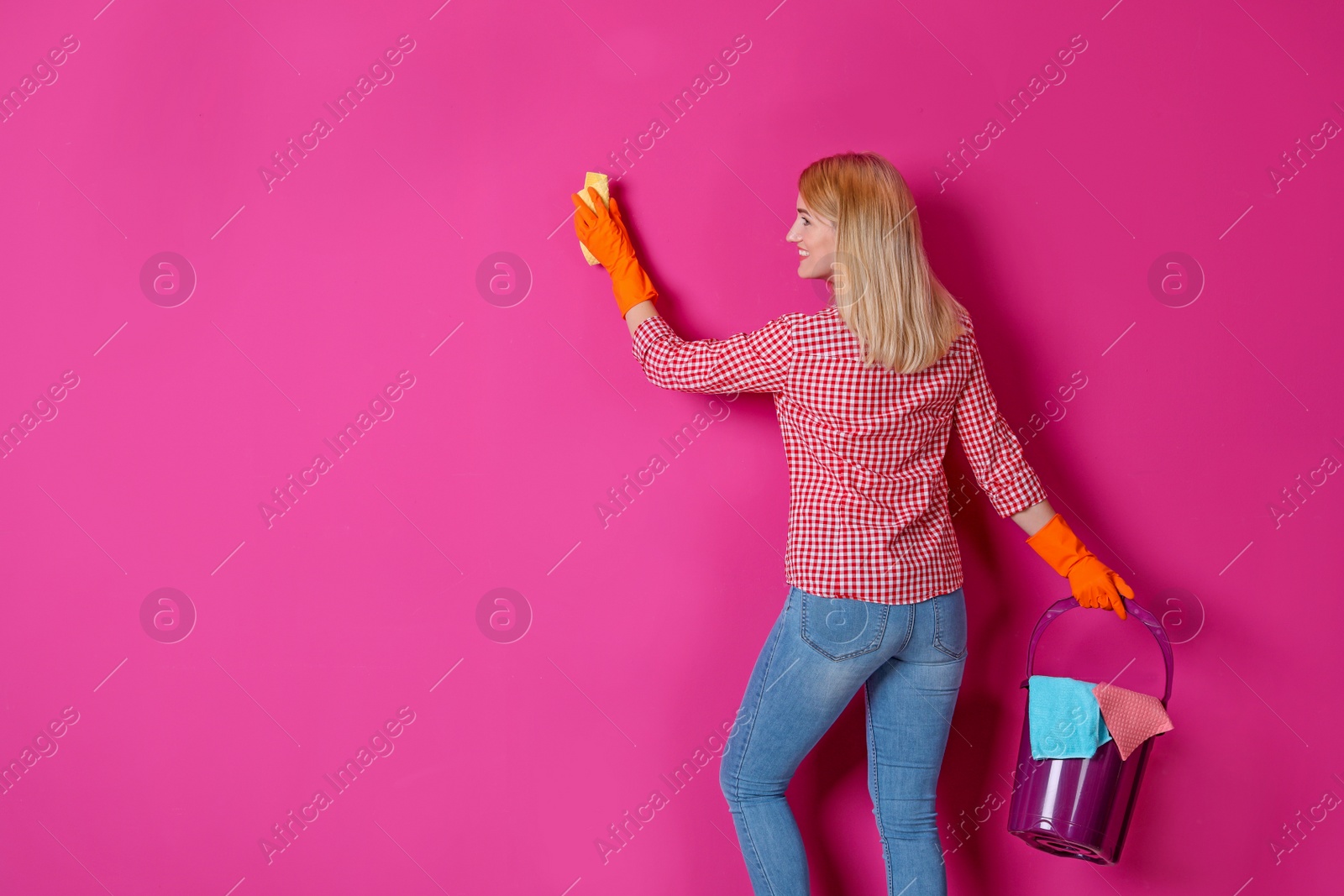 Photo of Woman in gloves cleaning color wall with rag