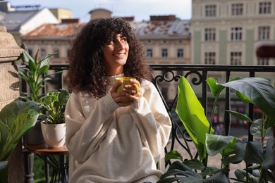 Photo of Beautiful young woman with cup of tea surrounded by houseplants on balcony