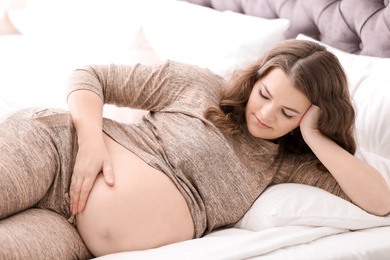 Photo of Young pregnant woman lying on bed at home