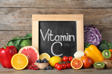 Photo of Different products and blackboard with phrase VITAMIN C on wooden table