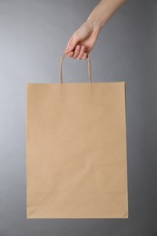 Photo of Woman holding kraft paper bag on grey background, closeup. Mockup for design