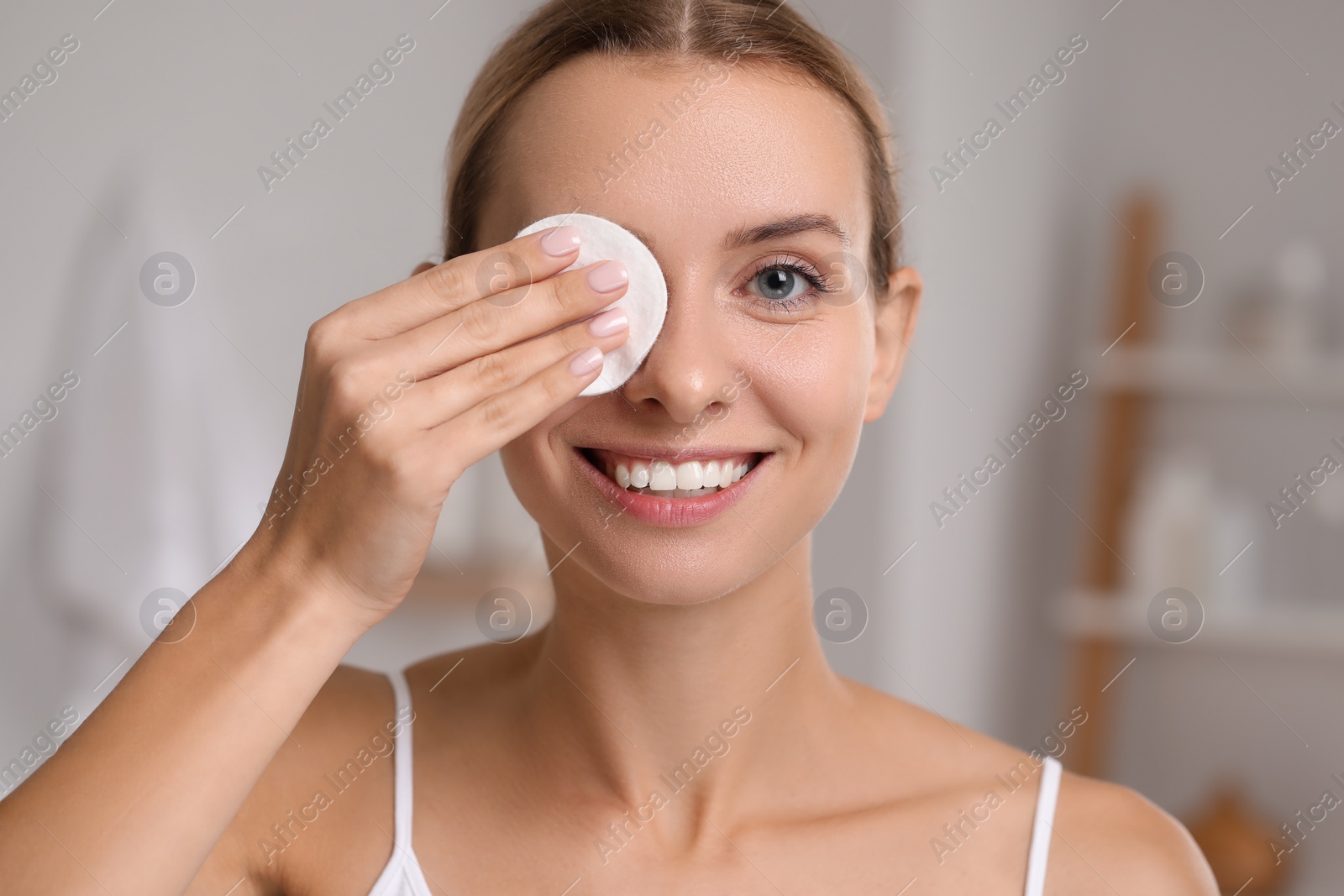 Photo of Smiling woman removing makeup with cotton pad indoors, closeup