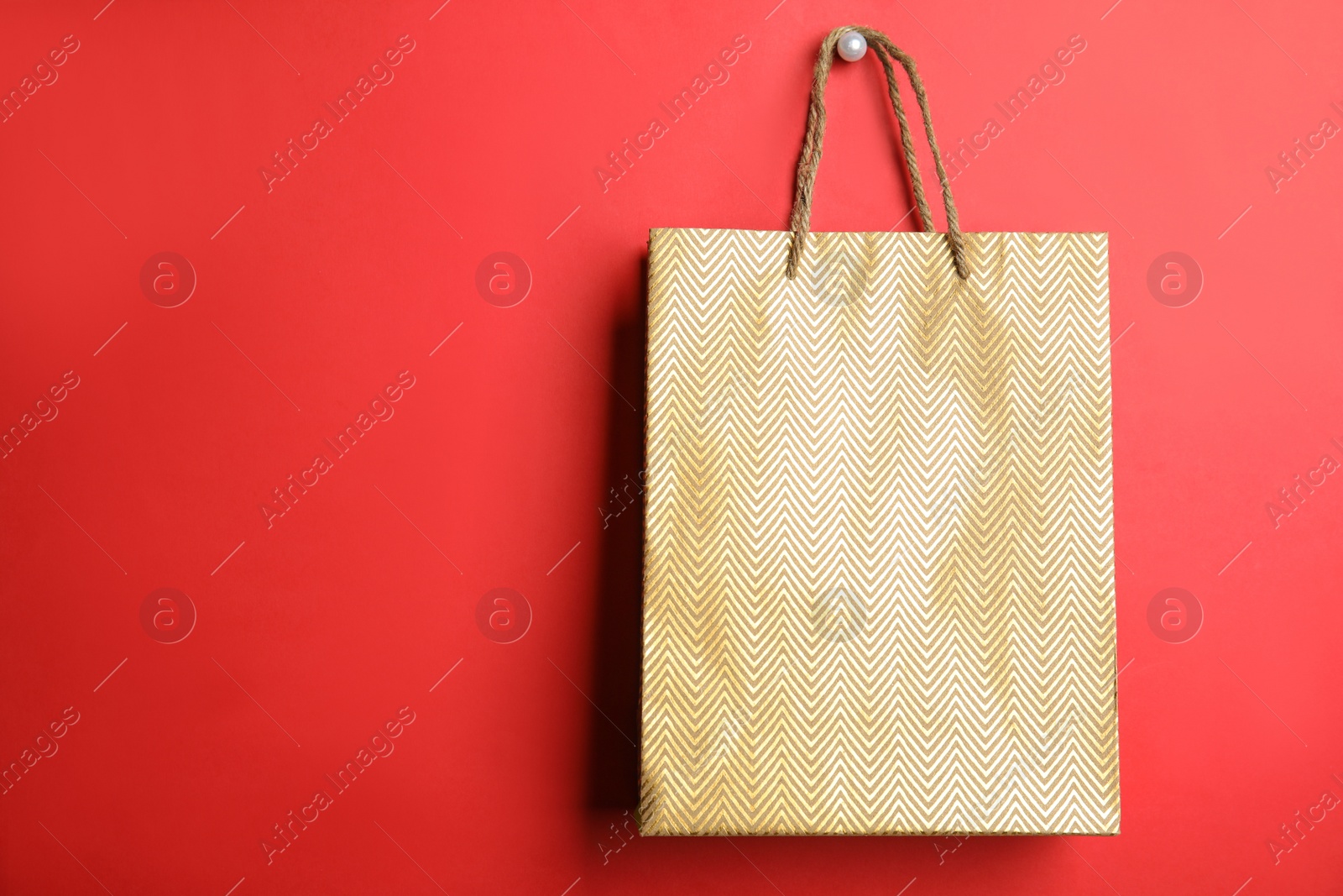 Photo of Gold shopping paper bag on red background, space for text