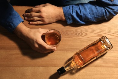 Photo of Addicted man with alcoholic drink at wooden table, top view