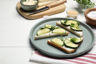 Photo of Tasty cucumber sandwiches with sesame seeds and pea microgreens on white wooden table, space for text
