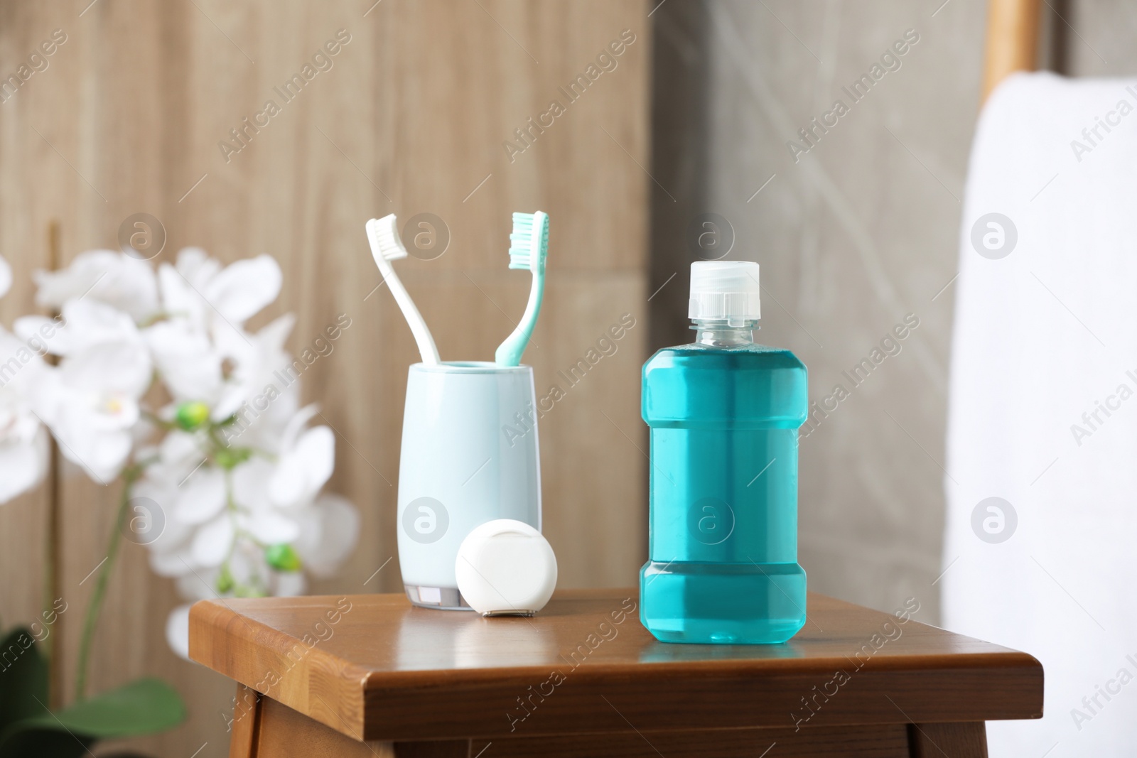 Photo of Bottle of mouthwash, toothbrushes and dental floss on wooden table in bathroom