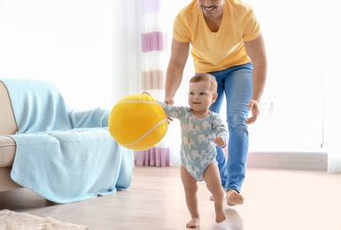 Photo of Baby and father playing with ball while learning to walk at home