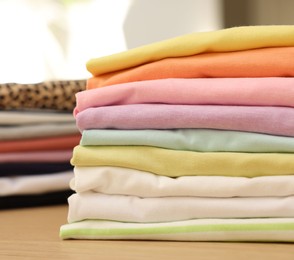 Photo of Many stacked clean clothes on wooden table, closeup