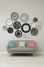 Sofa and many different clocks hanging on white wall in room