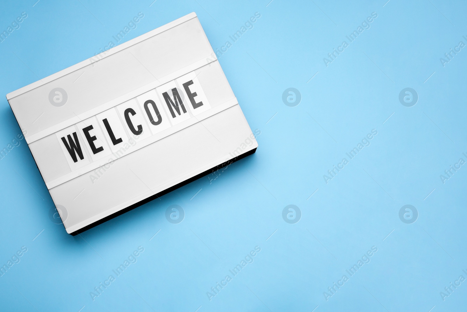 Photo of Lightbox with word Welcome on light blue background, top view. Space for text