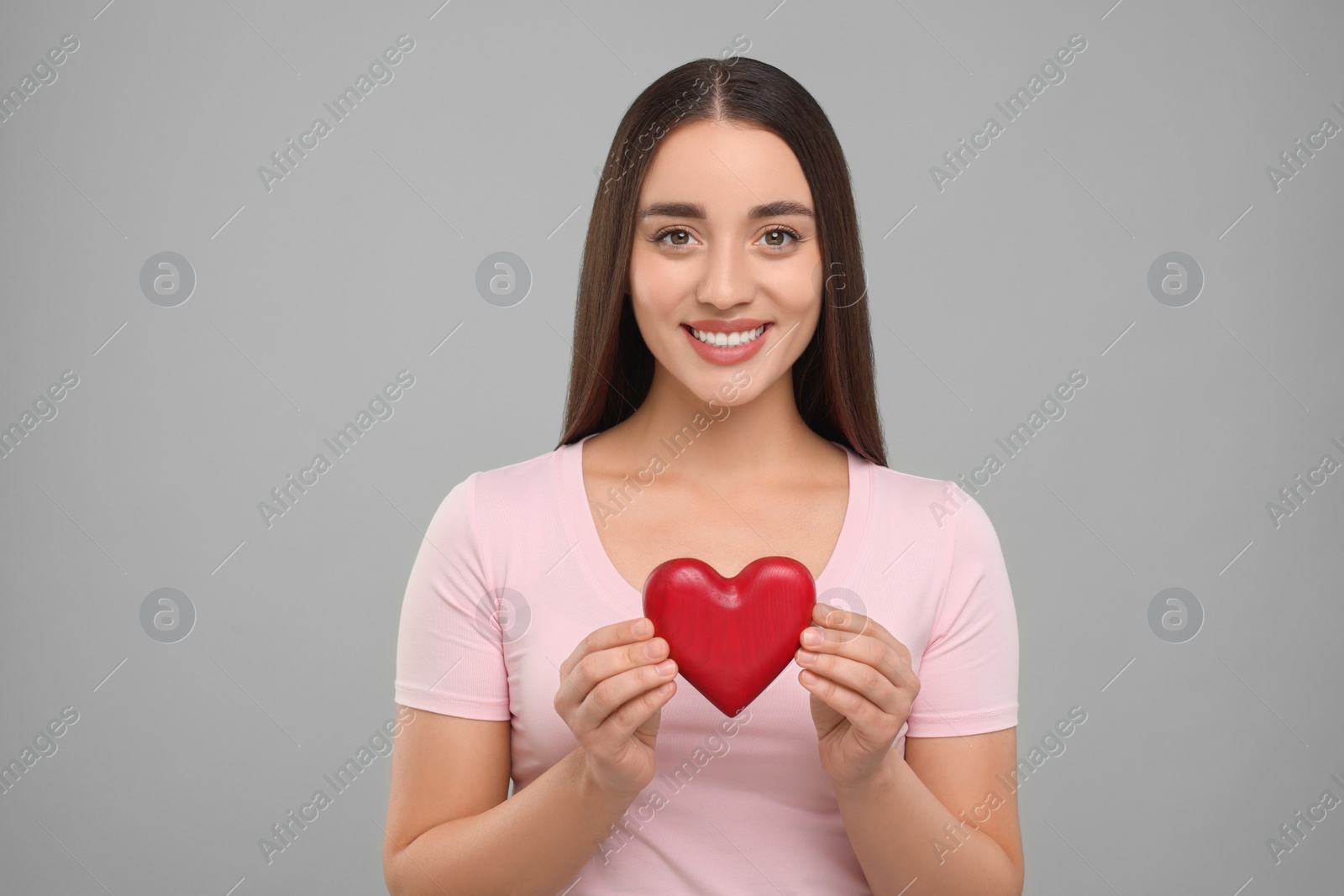 Photo of Happy young woman holding decorative red heart on light grey background