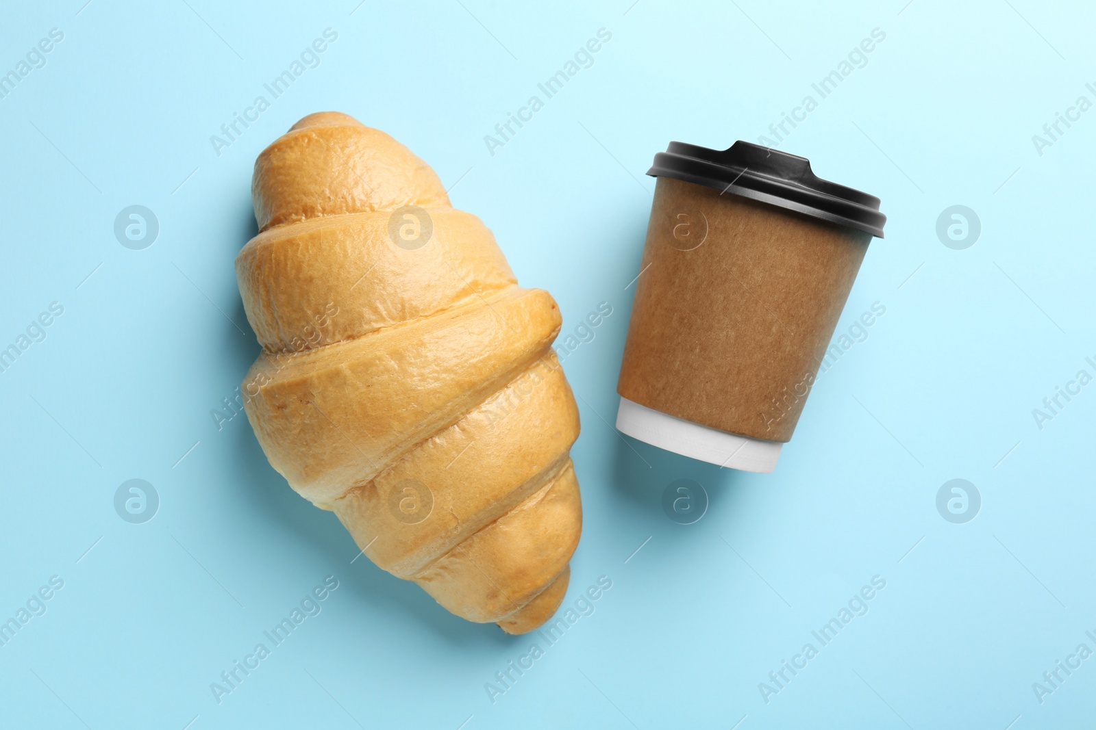 Photo of Delicious fresh croissant and paper cup with coffee on light blue table, flat lay