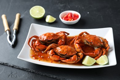 Photo of Delicious boiled crabs with sauce and lime on black textured table