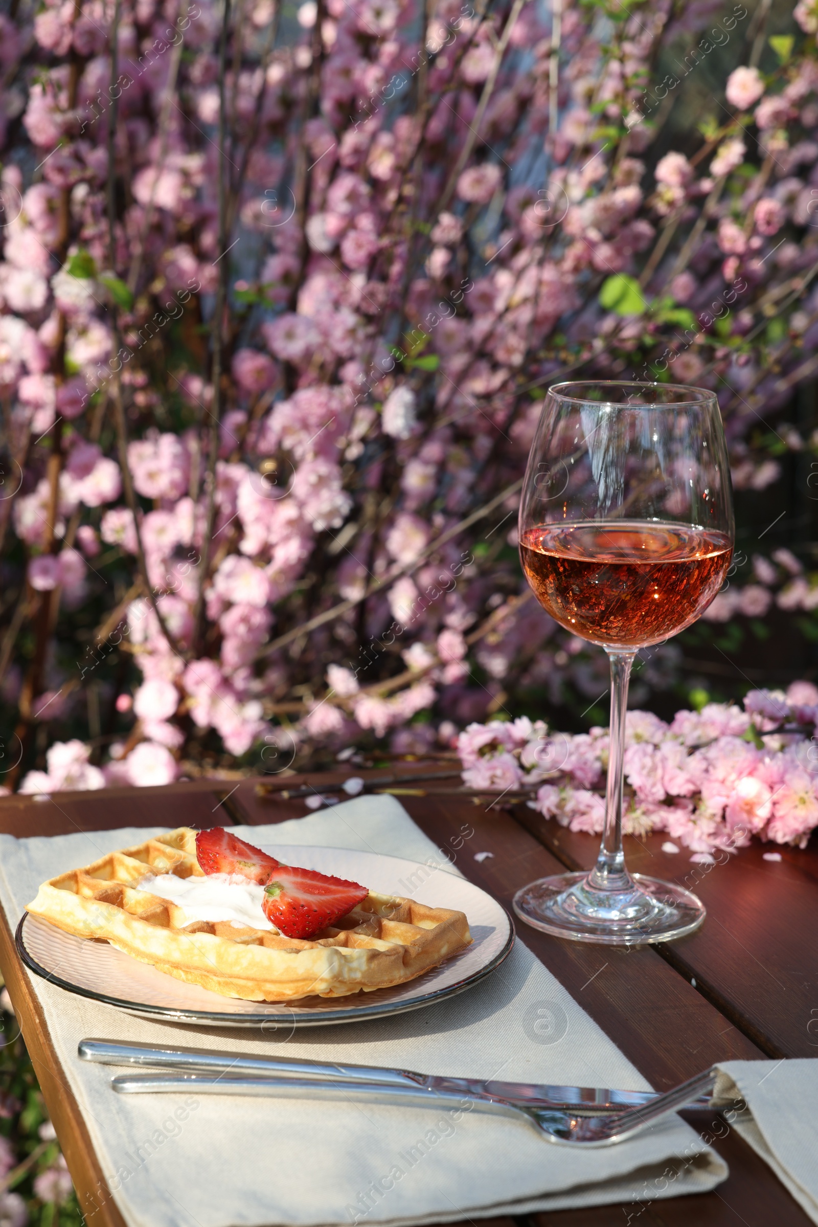 Photo of Delicious Belgian waffle with fresh strawberries and wine served on table in spring garden