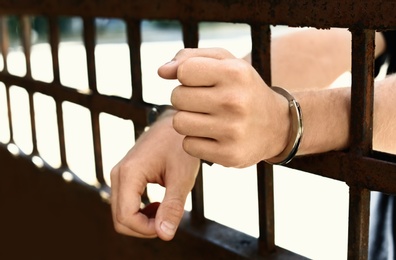 Photo of Man handcuffed in jail outdoors, closeup. Criminal law