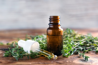 Photo of Bottle of essential oil with thyme on wooden table