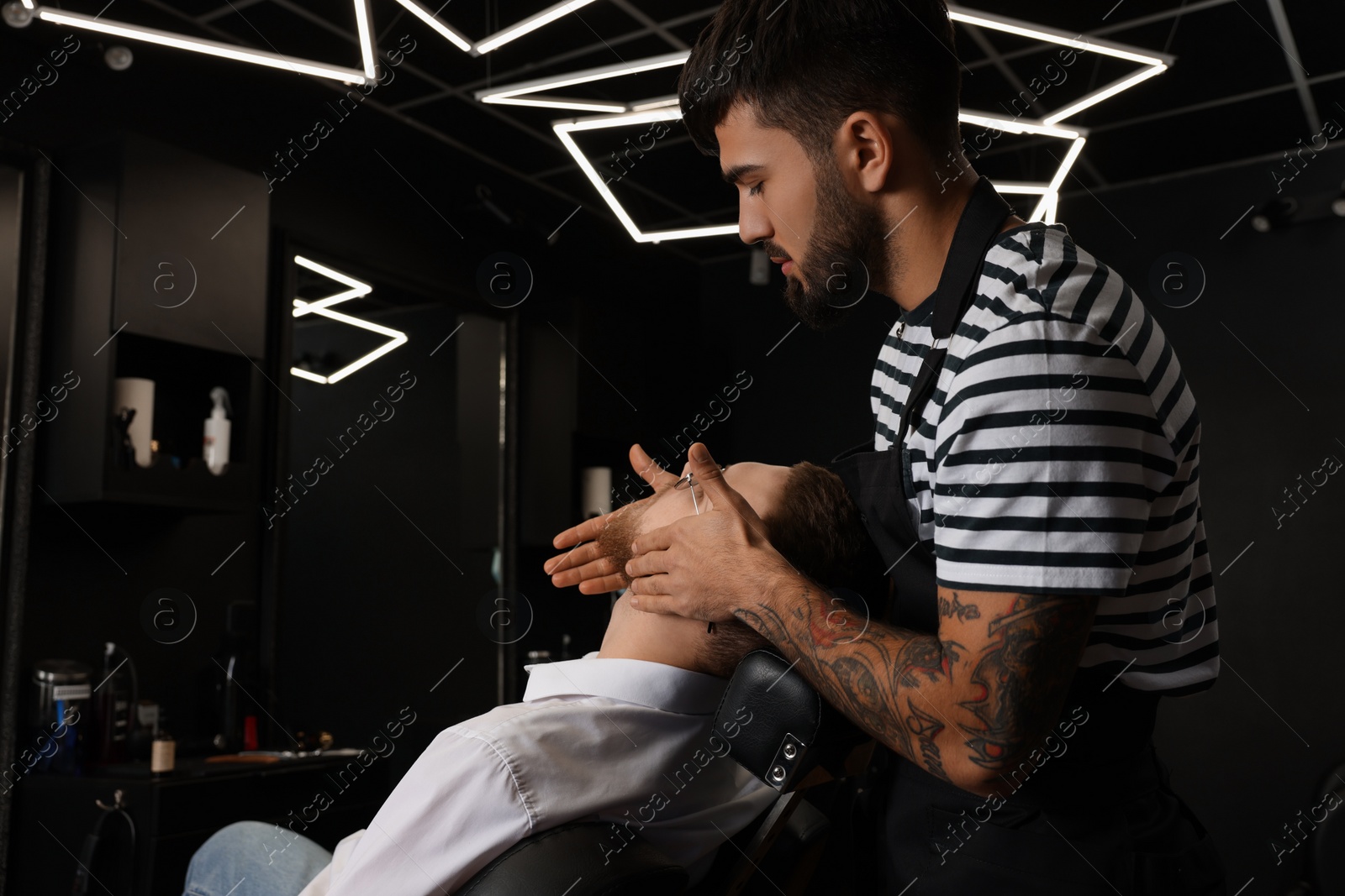 Photo of Hairdresser applying oil onto client's beard in barbershop. Professional shaving service