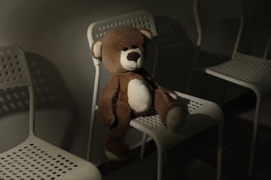 Photo of Cute lonely teddy bear on chair in dark room. Space for text