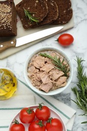 Bowl with canned tuna and products on white marble table, flat lay