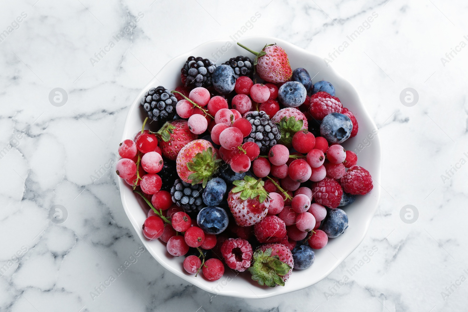 Photo of Mix of different frozen berries in bowl on white marble table, top view