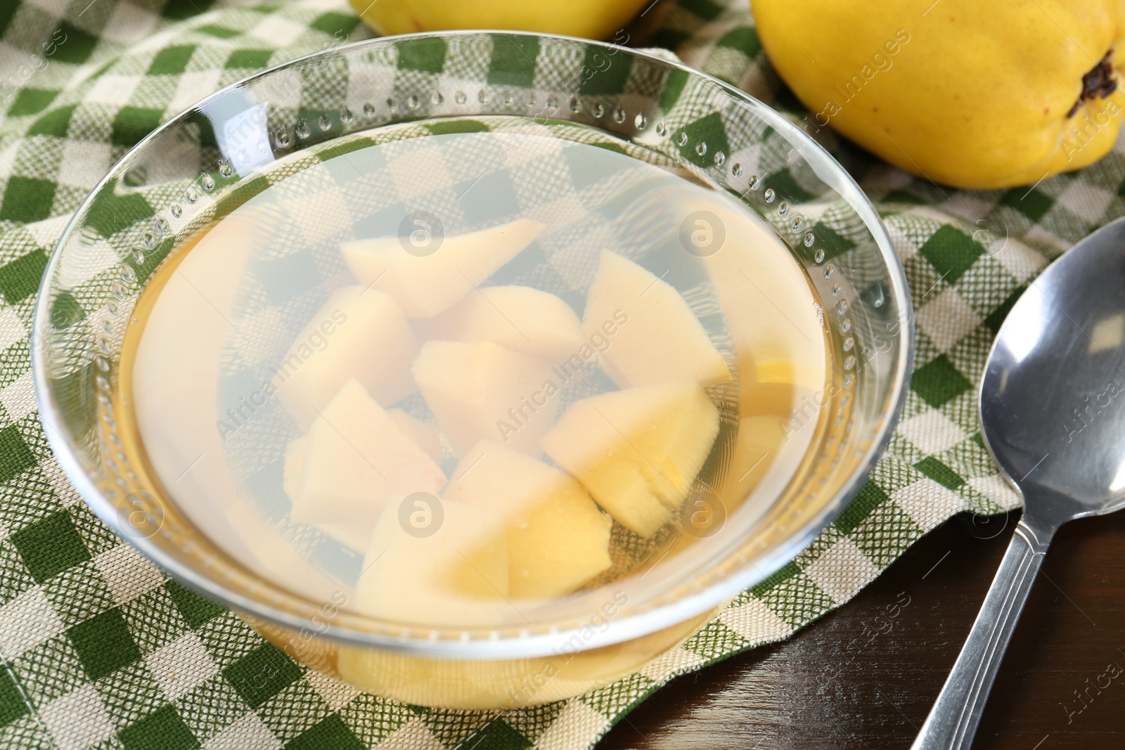 Photo of Delicious quince drink in glass bowl, fresh fruit and spoon on wooden table, closeup