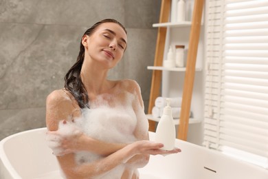 Photo of Woman taking bath with shower gel in bathroom, space for text