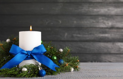 Photo of Burning white candle with Christmas decor on wooden table against dark background. Space for text